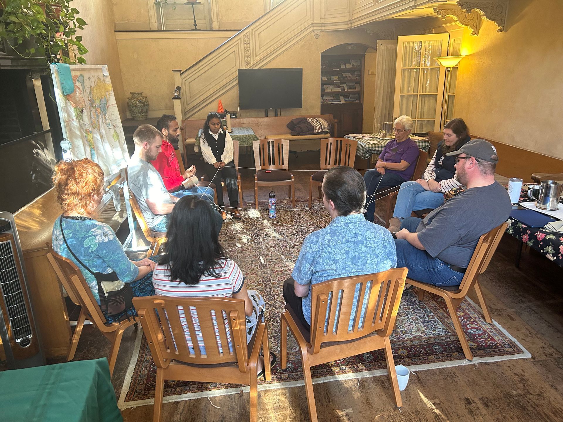 A group of people sit in a circle on wooden chairs in an indoor space, engaged in a discussion.