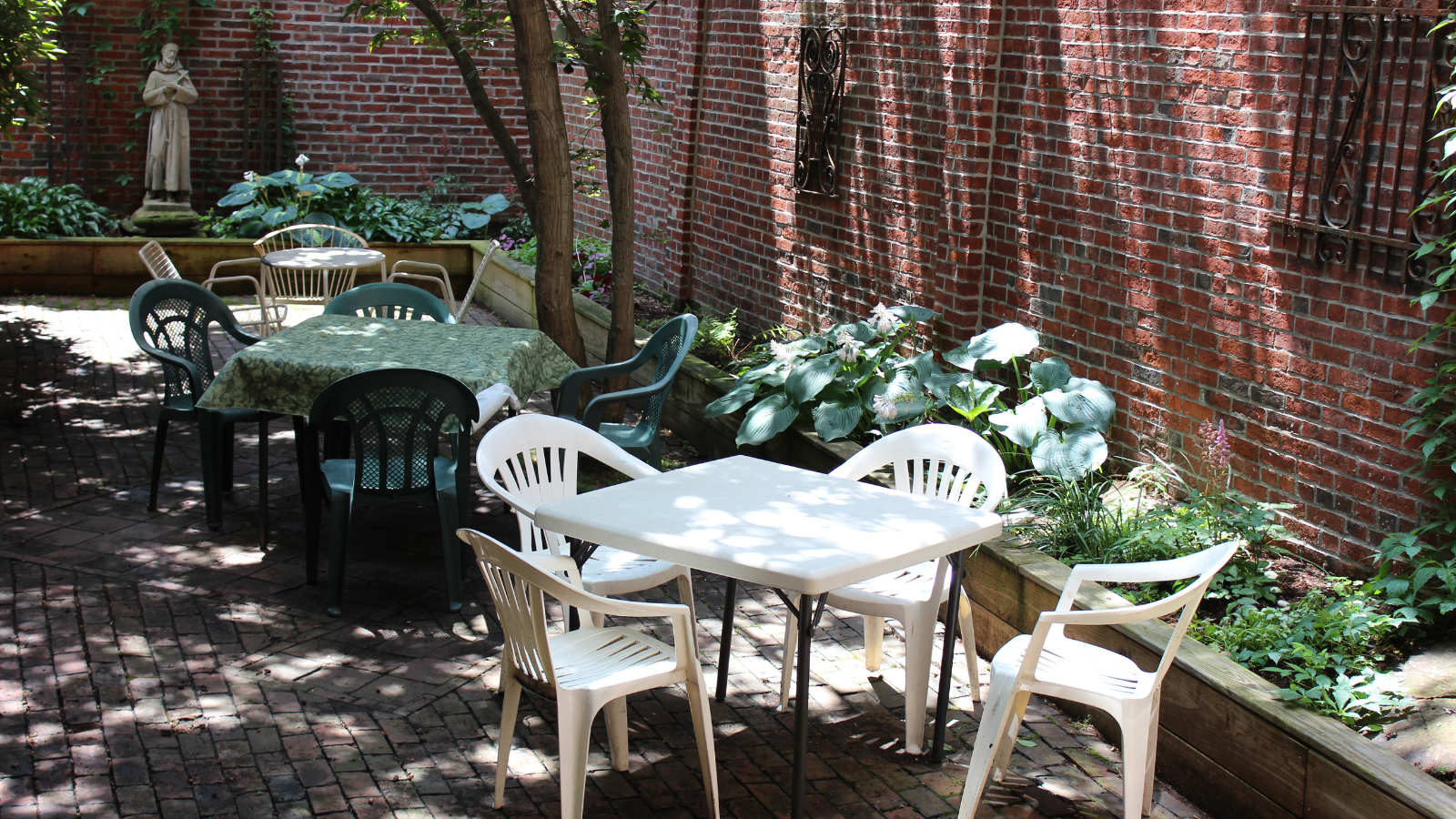 Outdoor dining area with tables and chairs near a brick wall and plants.