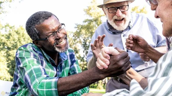 Three friends outdoors smiling and clasping hands in a playful group handshake