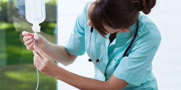 Nurse in teal scrubs adjusting an IV drip in a hospital setting