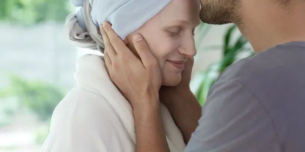 Two people facing each other closely, one gently cupping the other's face outdoors.