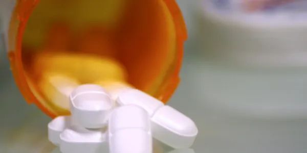 White pills spilling from an orange prescription bottle cap.