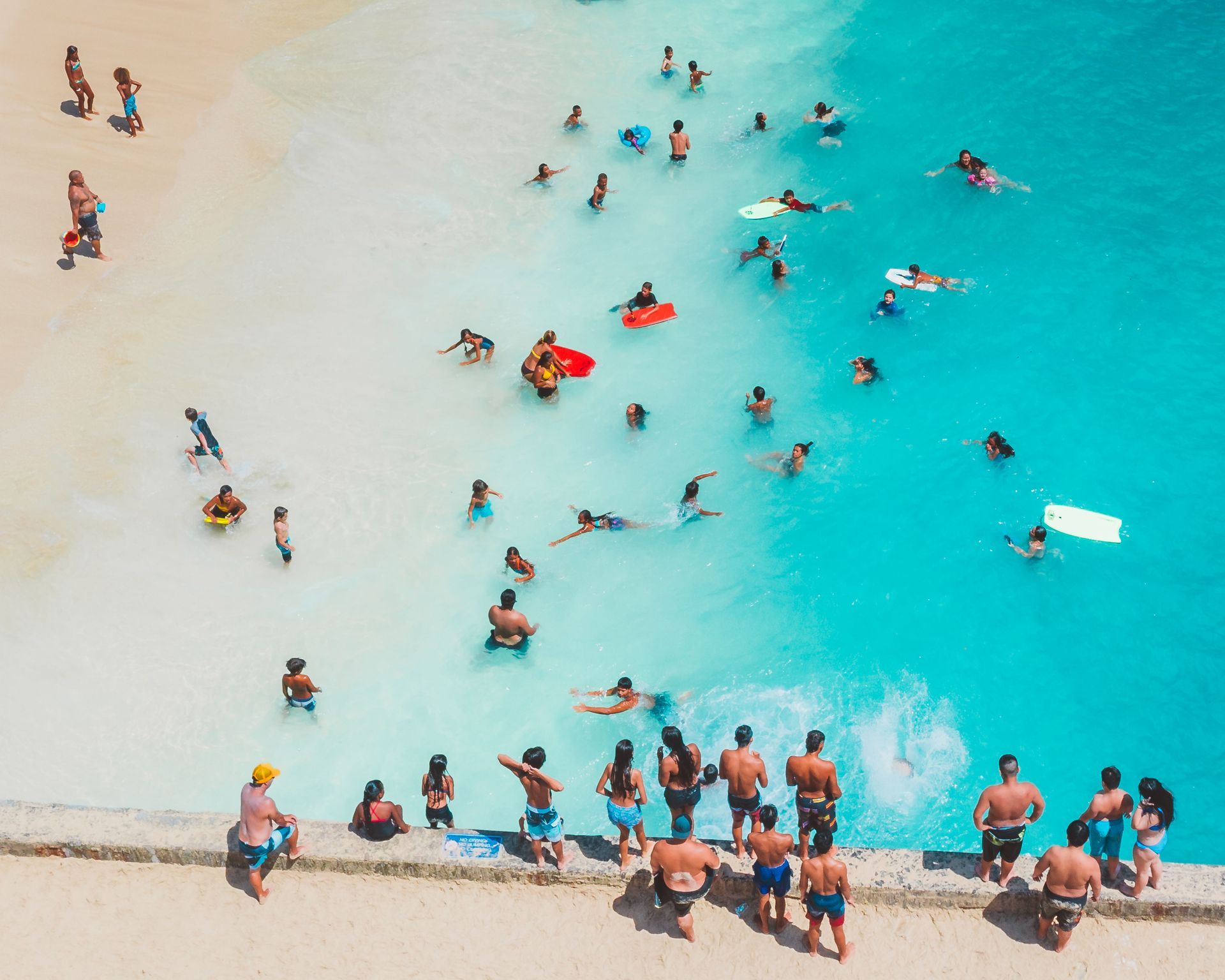 People wading and swimming in bright turquoise water at a crowded beach shore