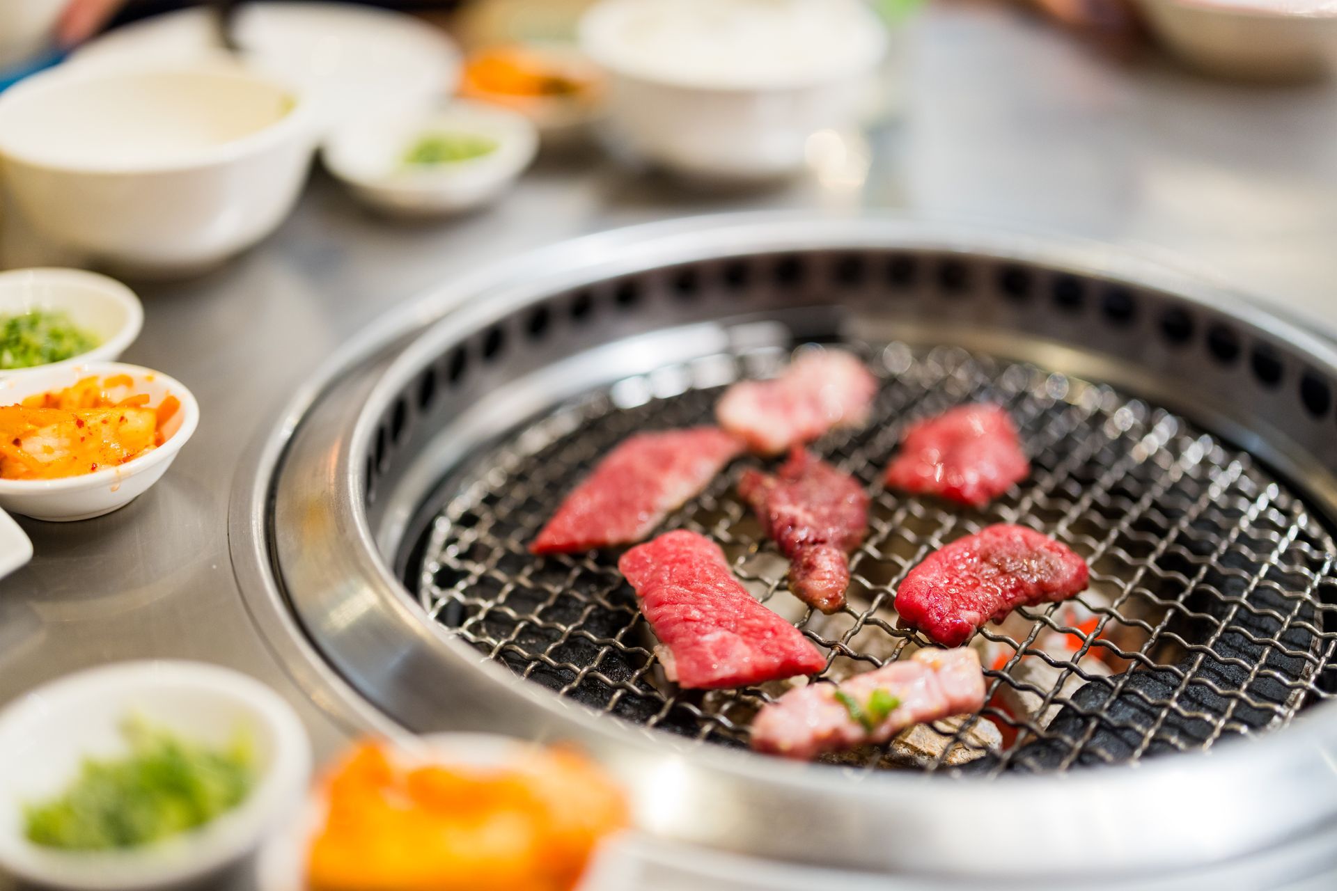JPOT Japanese BBQ with raw beef grilled on table grill with side dishes nearby in the background