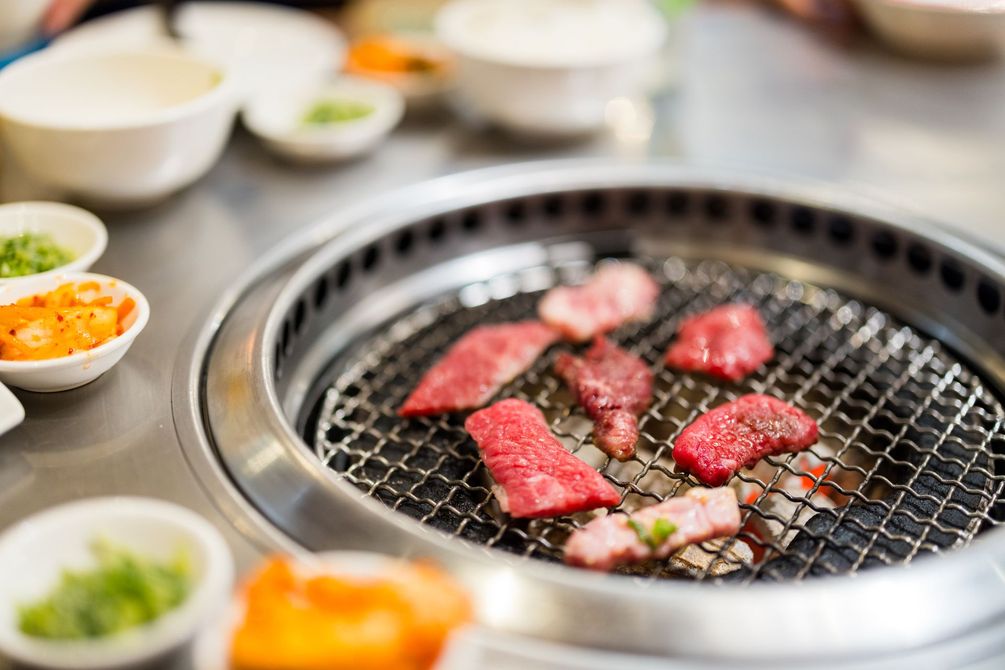 JPOT Japanese BBQ with raw beef grilled on table grill with side dishes nearby in the background