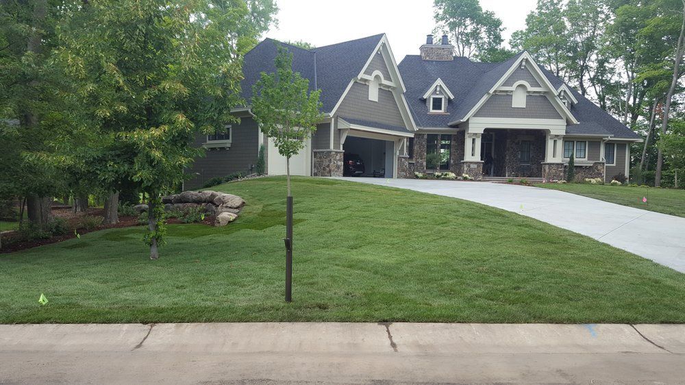 A single-story gray house with stone accents, a dark roof, and a fresh green lawn, viewed from the street.