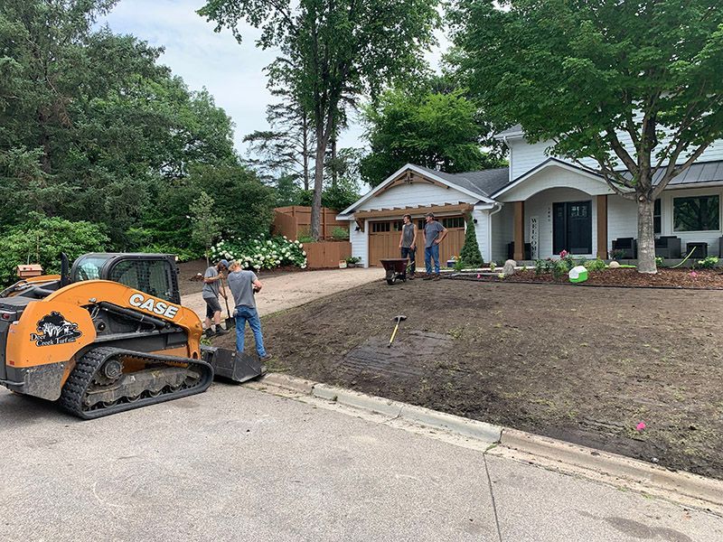 Construction workers landscaping a residential front yard with a Case skid steer loader.