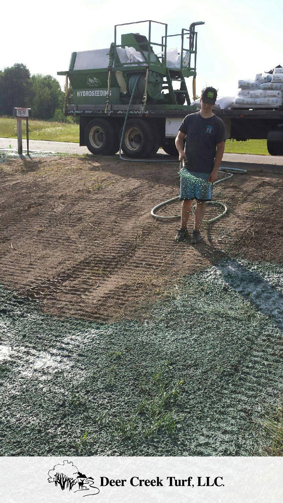 A worker sprays green hydroseed onto a dirt slope from a truck at Deer Creek Turf, LLC.