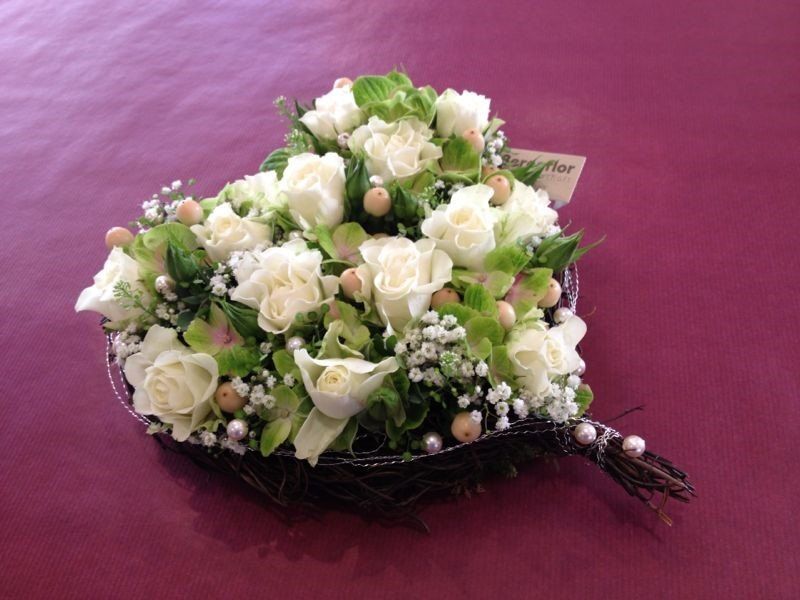 Ein herzförmiges Arrangement aus weißen Rosen und Schleierkraut auf einem roten Tisch.