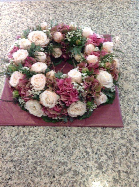 Auf einem Tisch steht ein Kranz aus rosa und weißen Blumen.