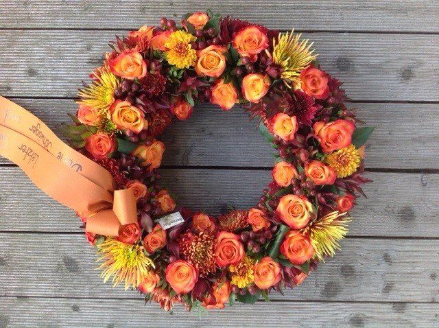 Auf einem Holztisch steht ein Kranz aus orangefarbenen und gelben Blumen.