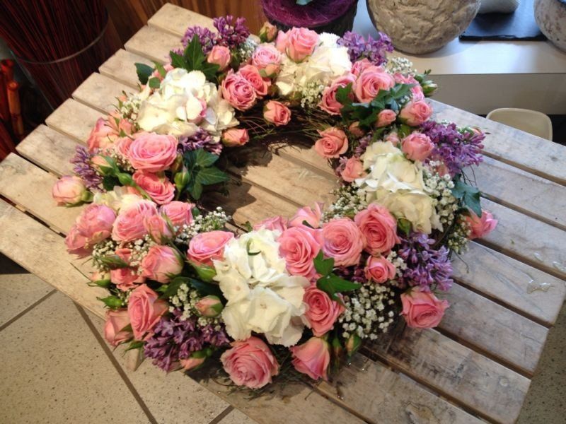 Auf einem Holztisch steht ein Kranz aus rosa und weißen Blumen.