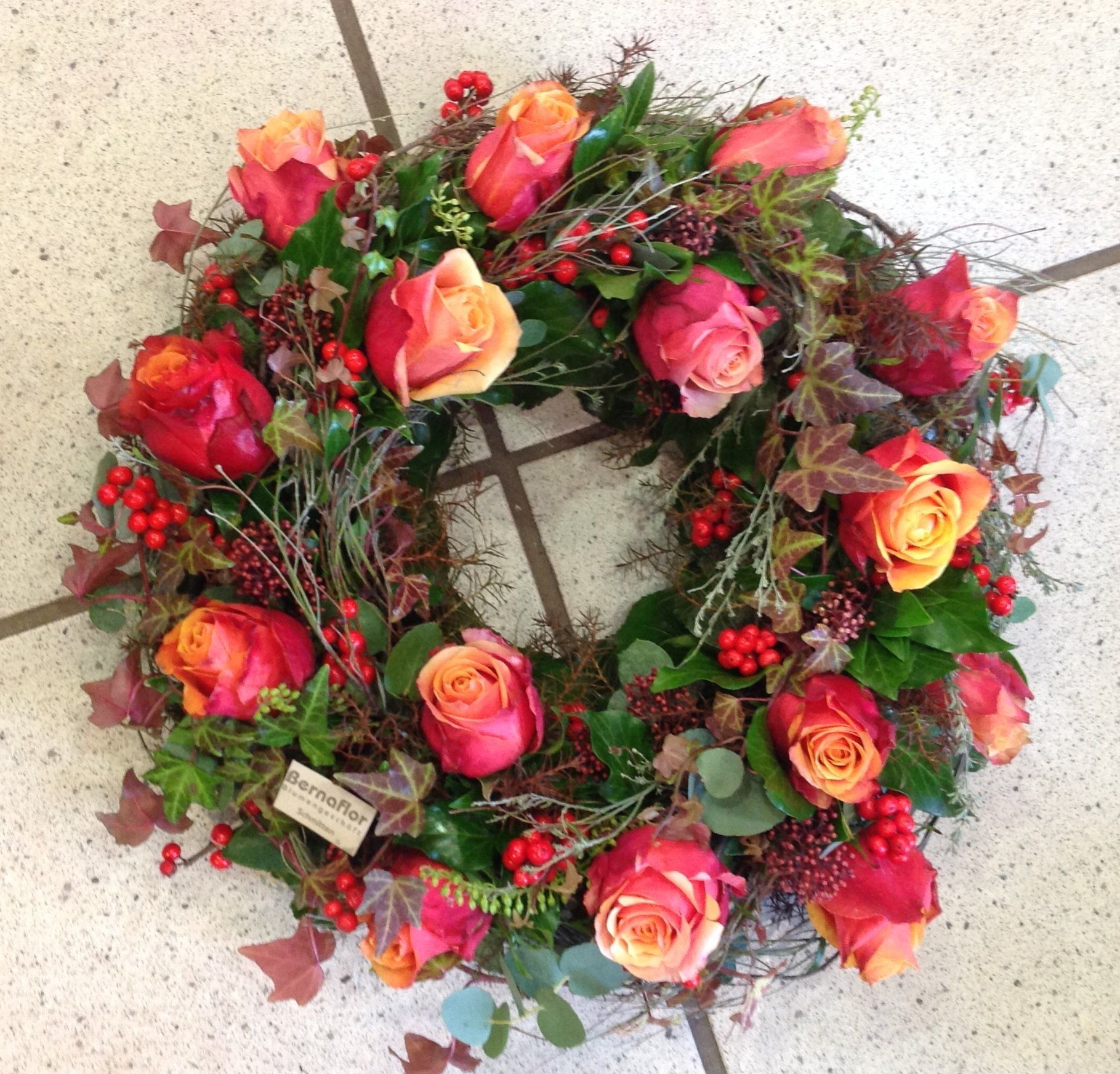 Ein Kranz aus roten und orangefarbenen Rosen und Beeren auf einem gefliesten Boden
