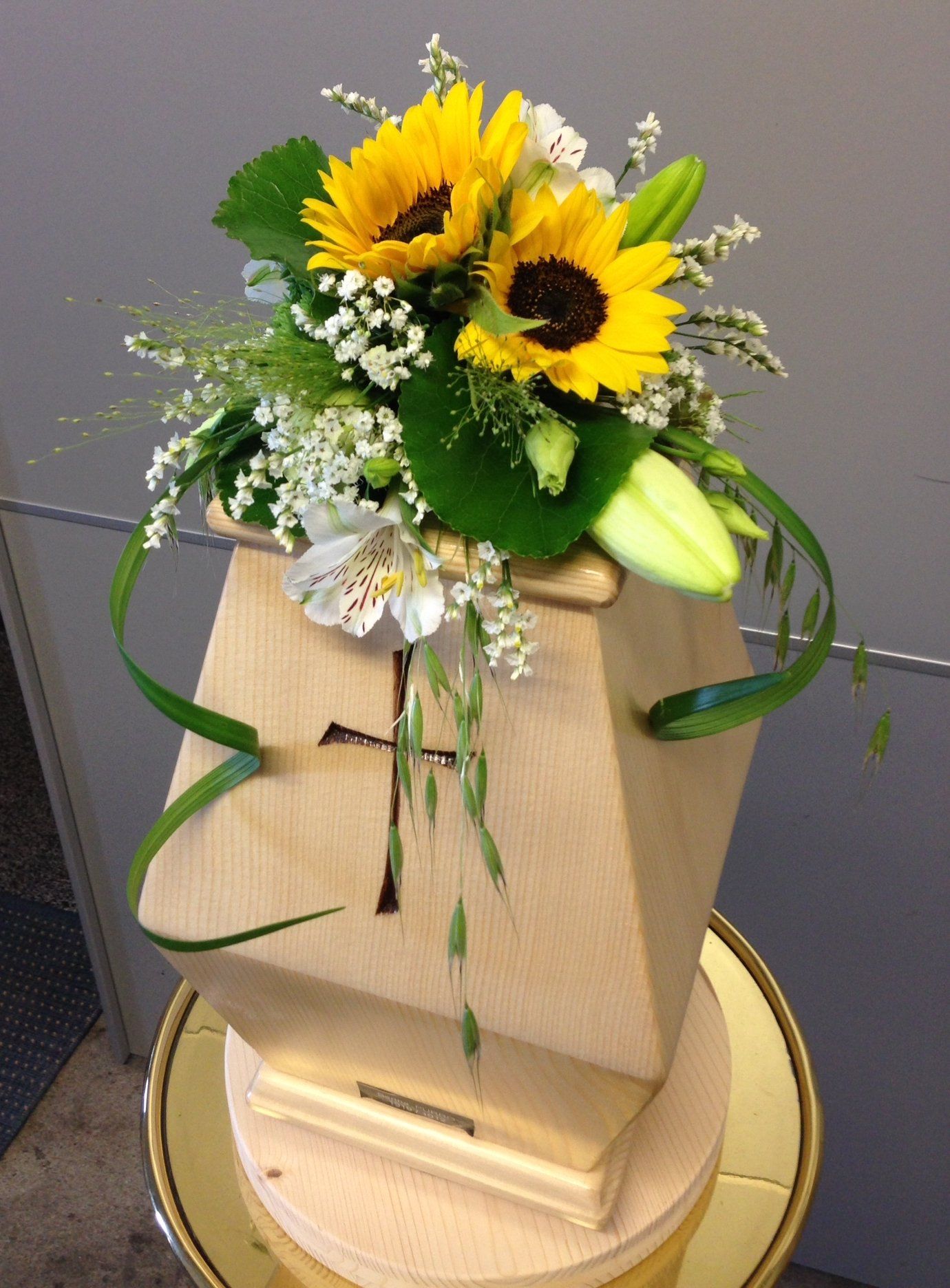 Eine hölzerne Urne mit Sonnenblumen und Lilien darauf