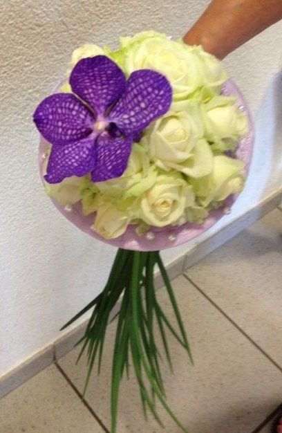 Eine Person hält einen Strauß weißer Rosen und einer lila Blume