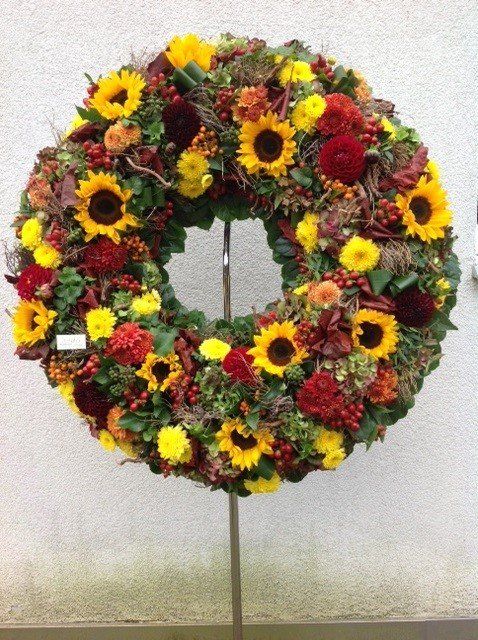 Ein Kranz mit Sonnenblumen und roten Blumen auf einem Ständer