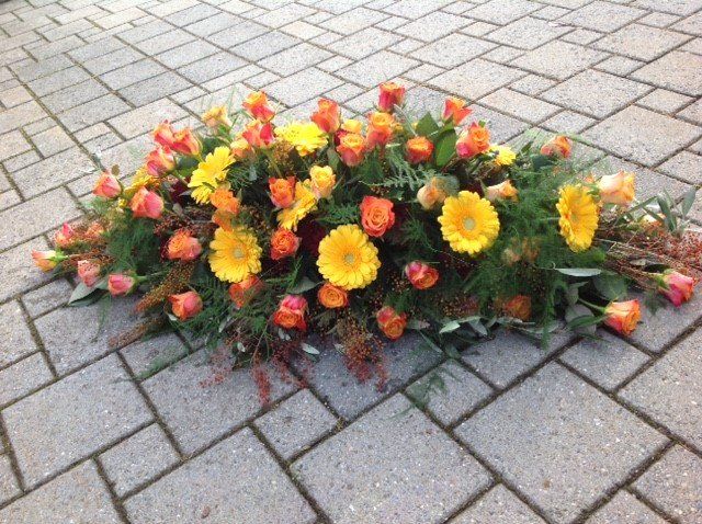 Auf einem gepflasterten Gehweg liegt ein Strauß gelber und orangefarbener Blumen.
