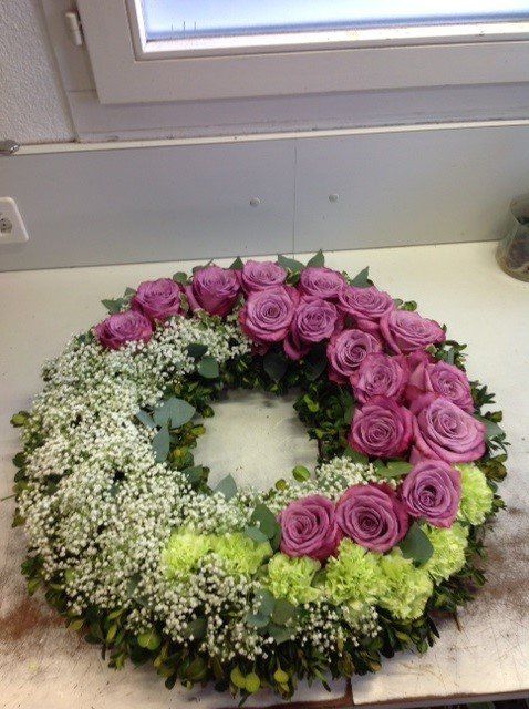 Ein Kranz mit rosa Rosen und grünen Blumen auf einem Tisch