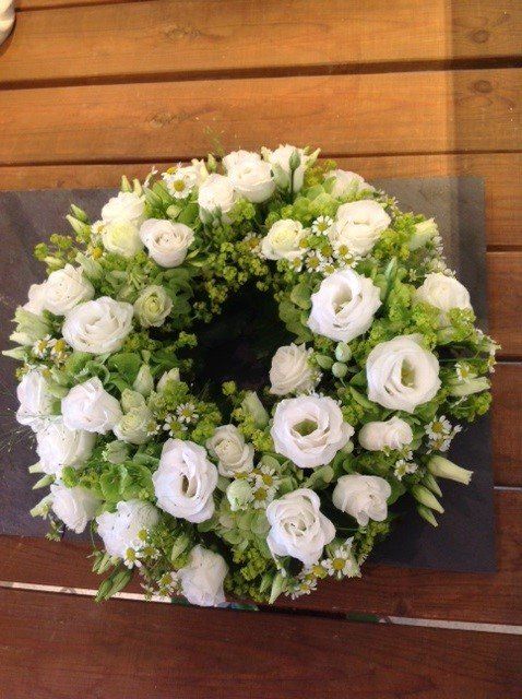 Auf einem Holztisch steht ein Kranz aus weißen und grünen Blumen.