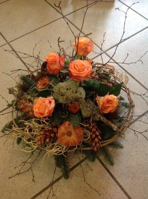 Ein Strauß orangefarbener Rosen und Tannenzapfen auf einem gefliesten Boden