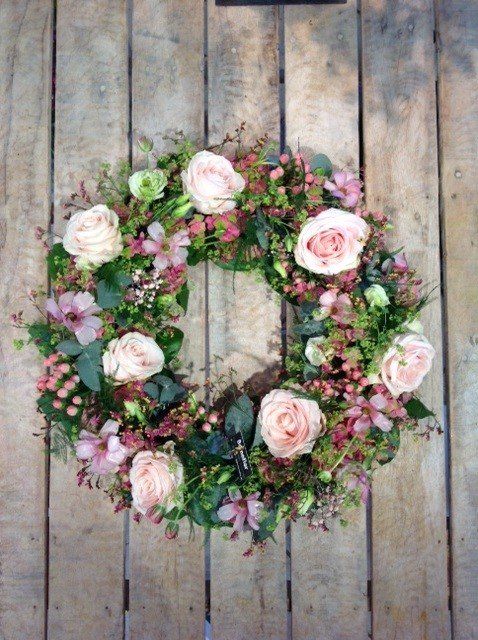Auf einem Holztisch steht ein Kranz aus rosa Rosen.