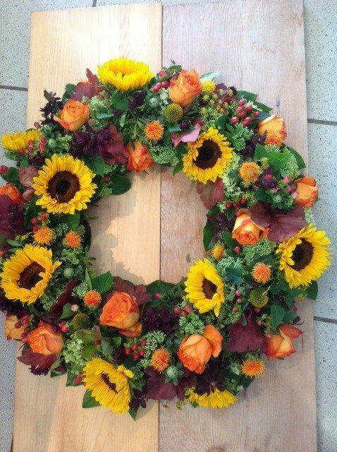 Ein Kranz aus Sonnenblumen und Rosen liegt auf einem Holztisch