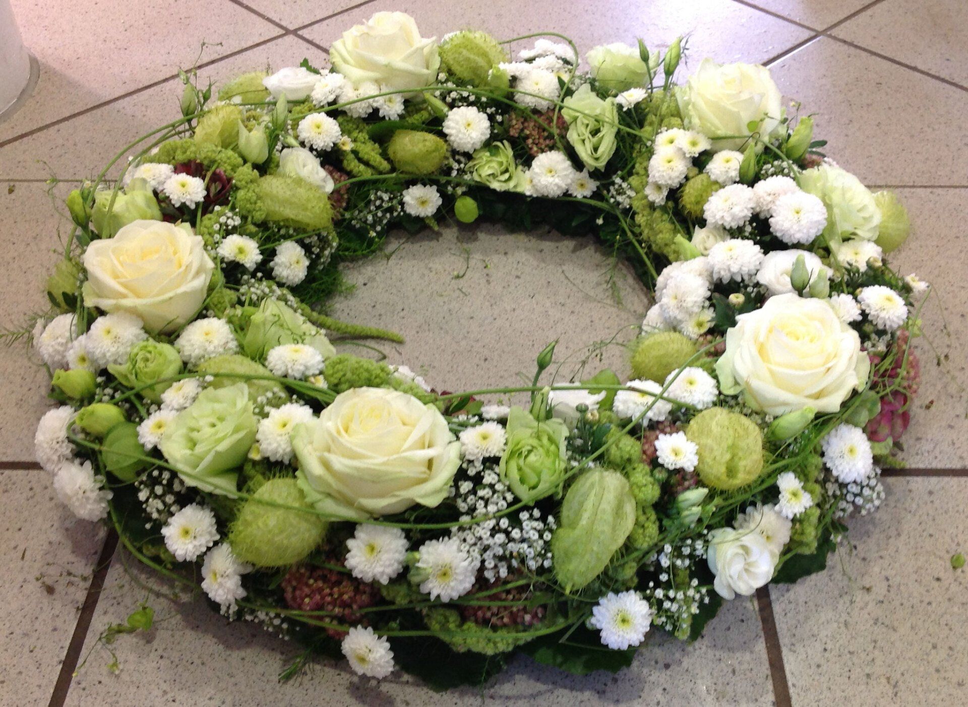 Auf einem gefliesten Boden liegt ein Kranz aus weißen und grünen Blumen.