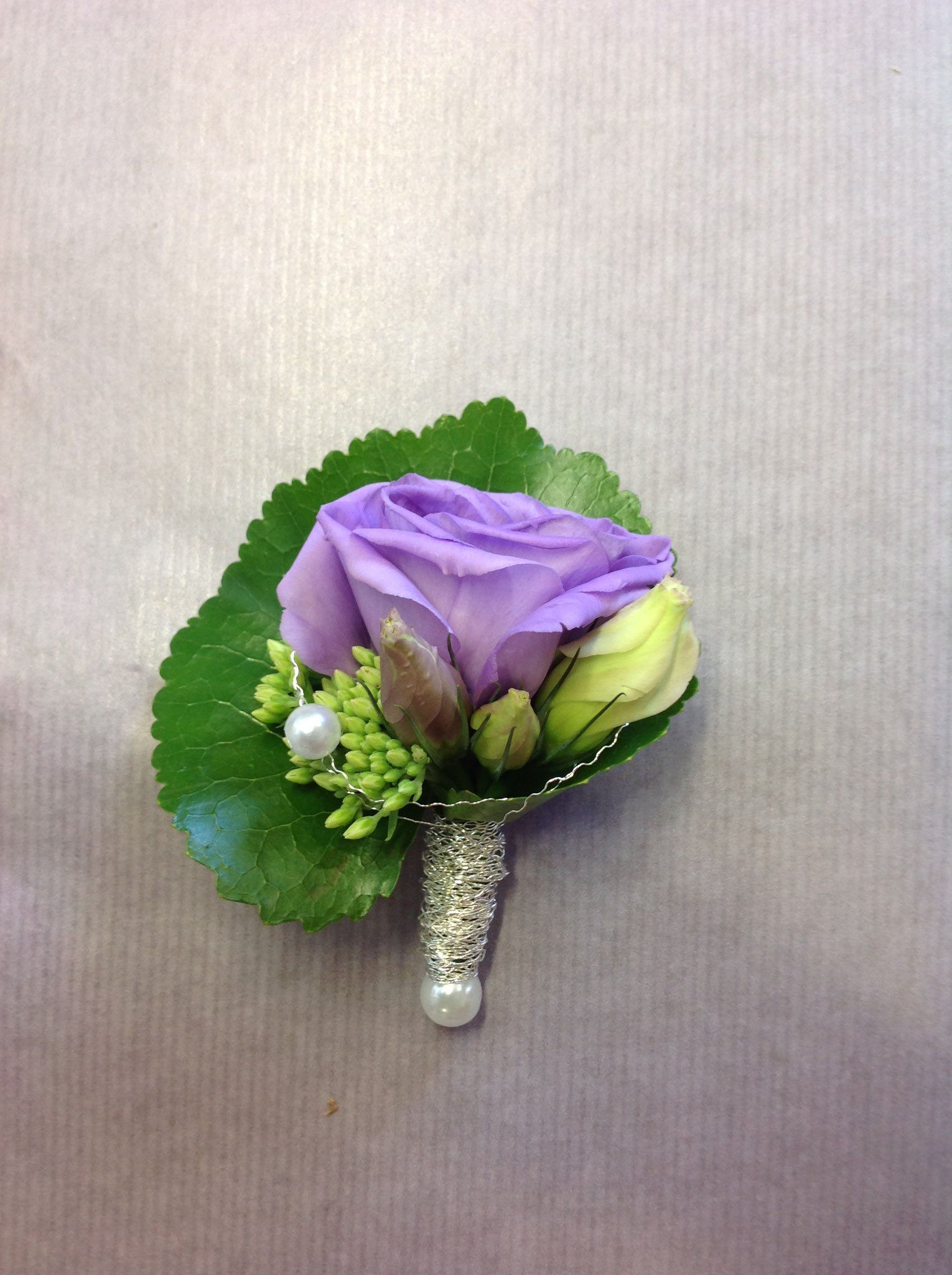 Eine violette Rose mit grünen Blättern und einer Perle auf einem Tisch.