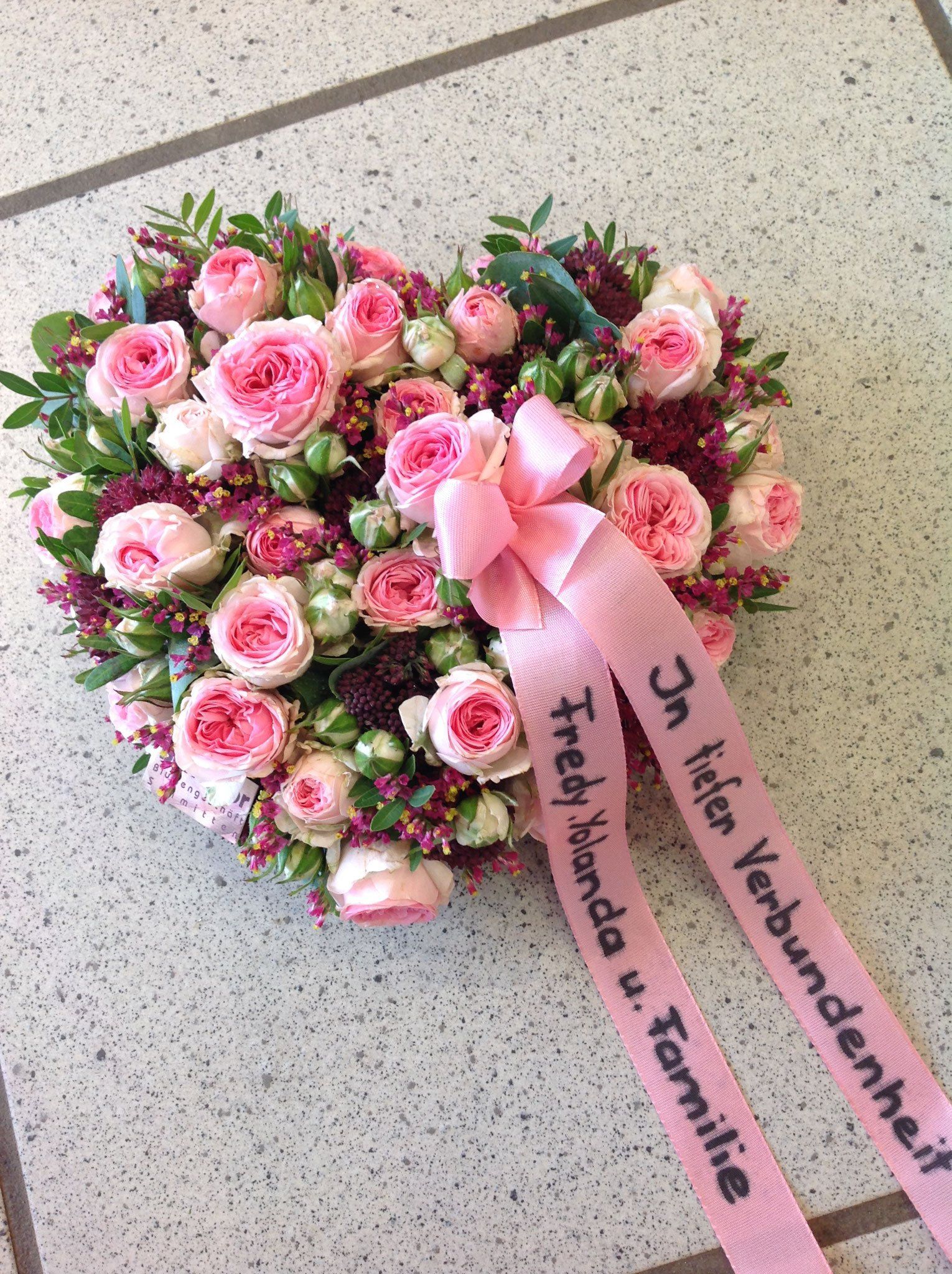 Ein herzförmiger Kranz aus rosa Rosen mit einer rosa Schleife.