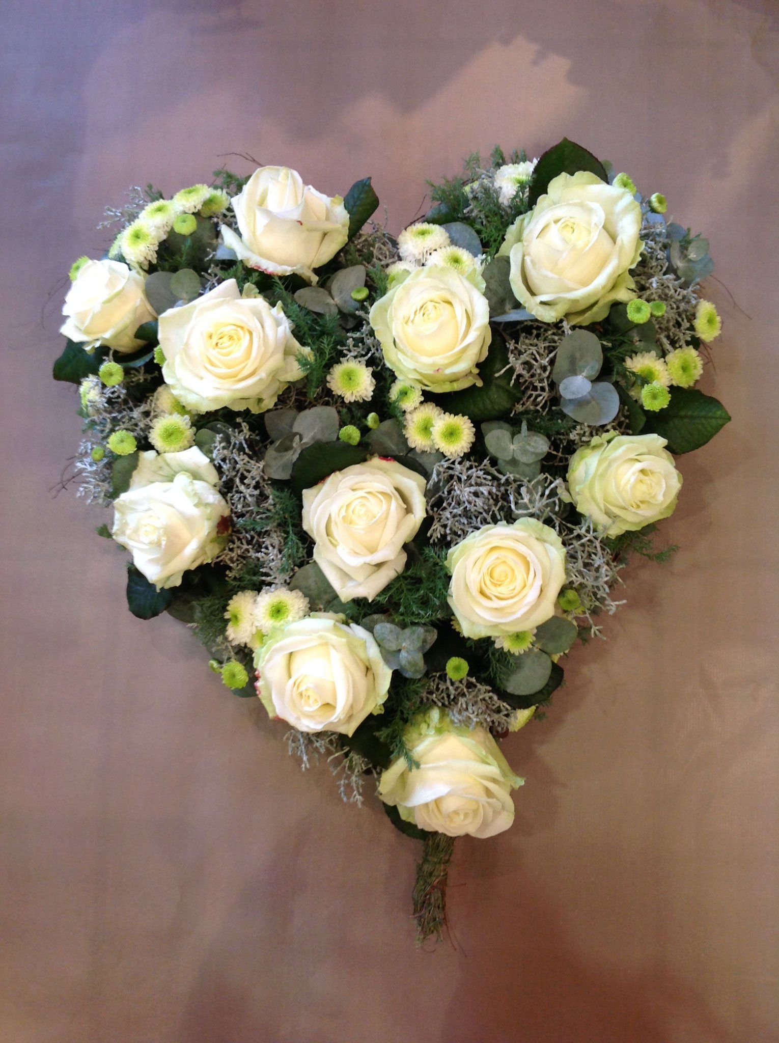 Ein herzförmiges Arrangement aus weißen Rosen und Grünpflanzen auf einem Tisch.