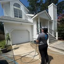 A person is spraying water on the side of a house.