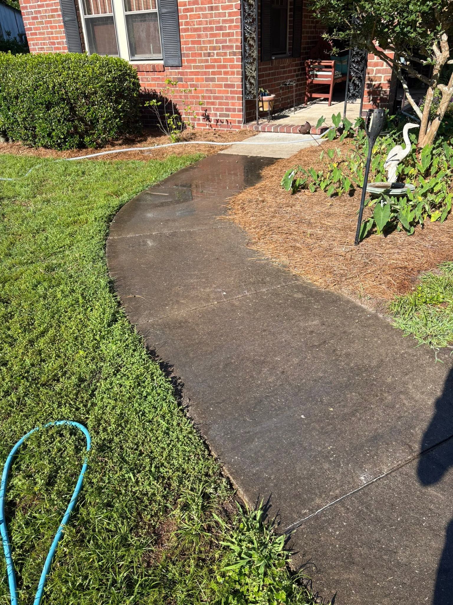 A person is using a high pressure washer to clean a sidewalk.