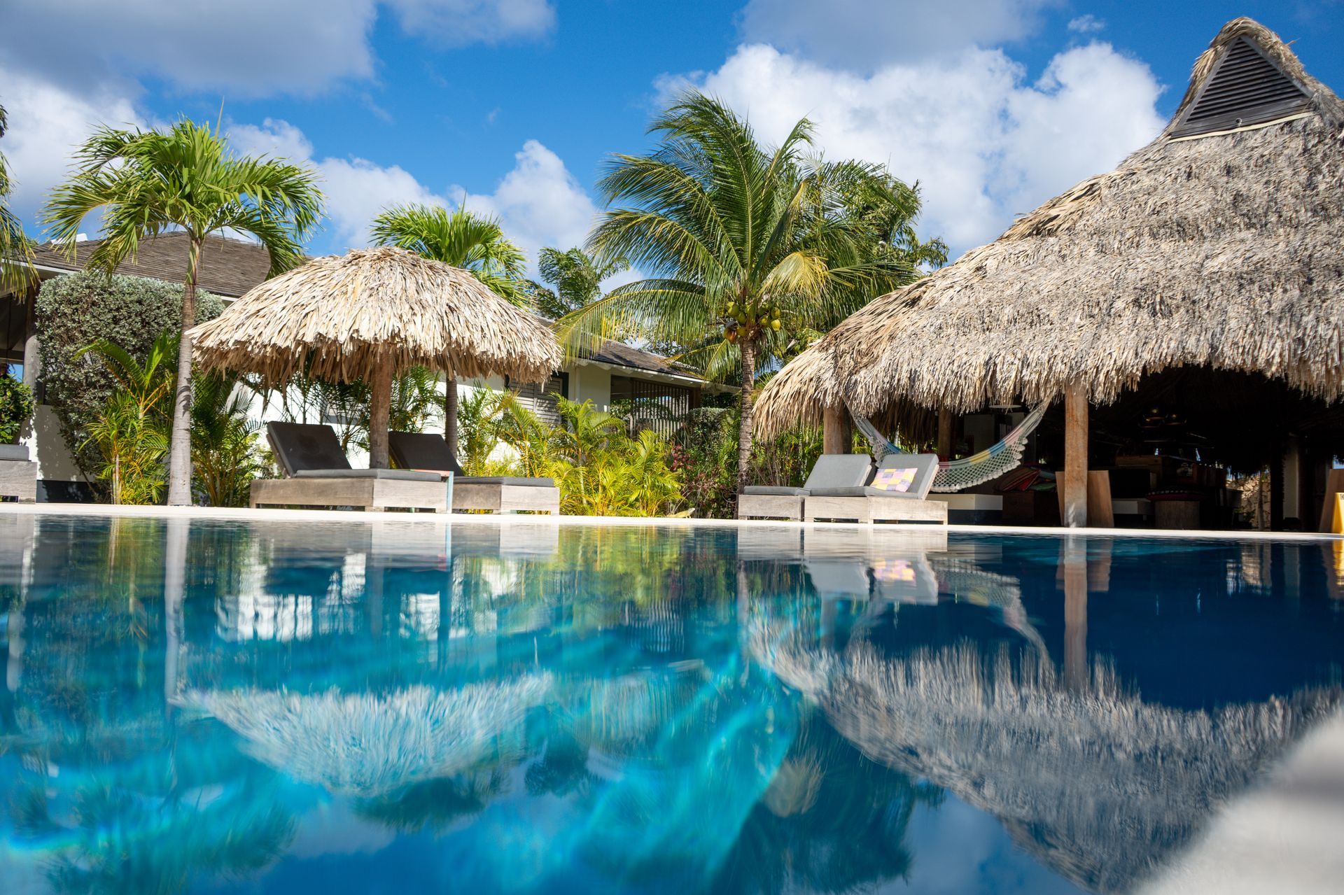 A large swimming pool surrounded by thatched umbrellas and chairs.