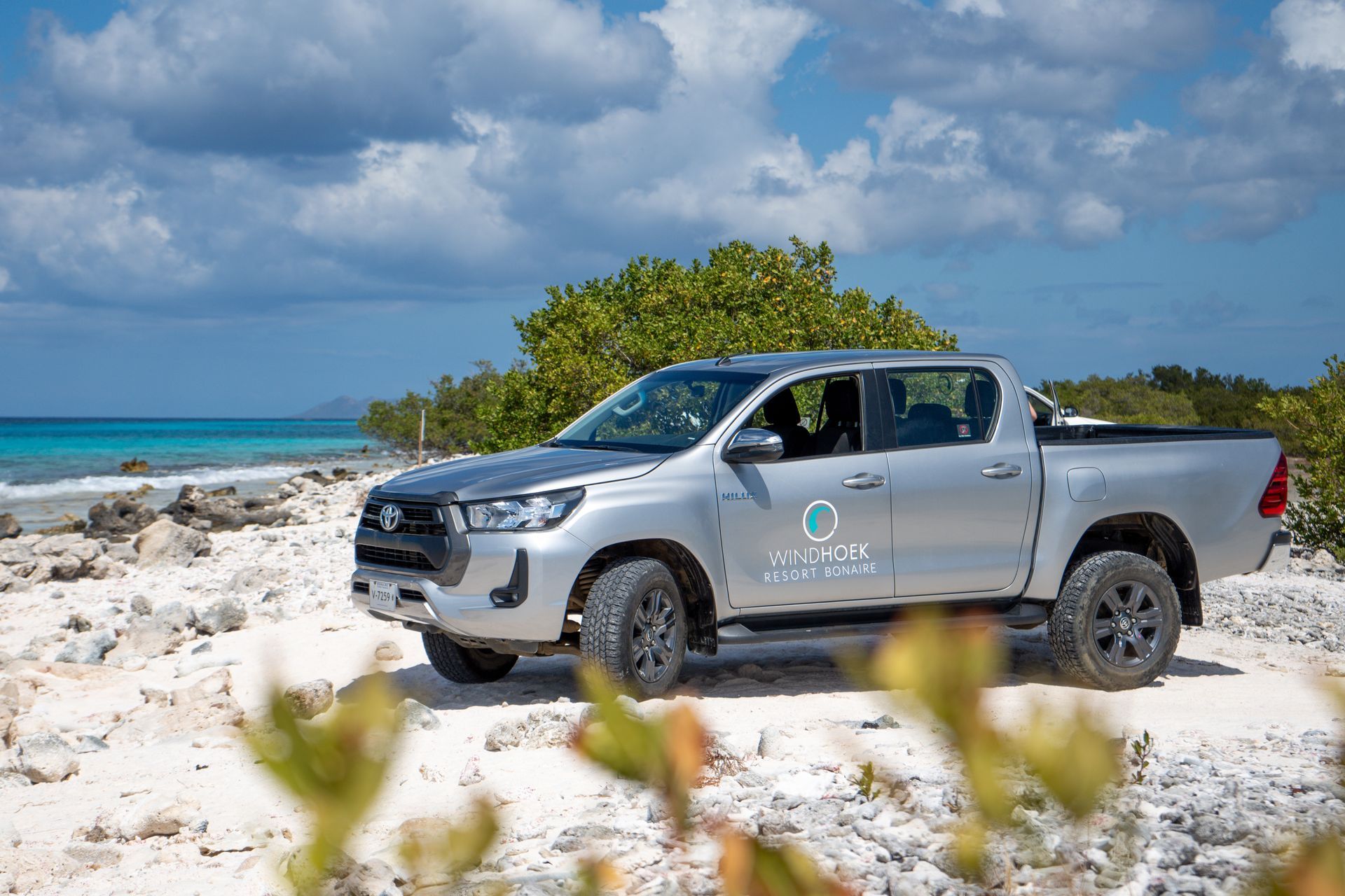 A silver Windhoek Resort pickup truck is parked on a sandy beach near the ocean.