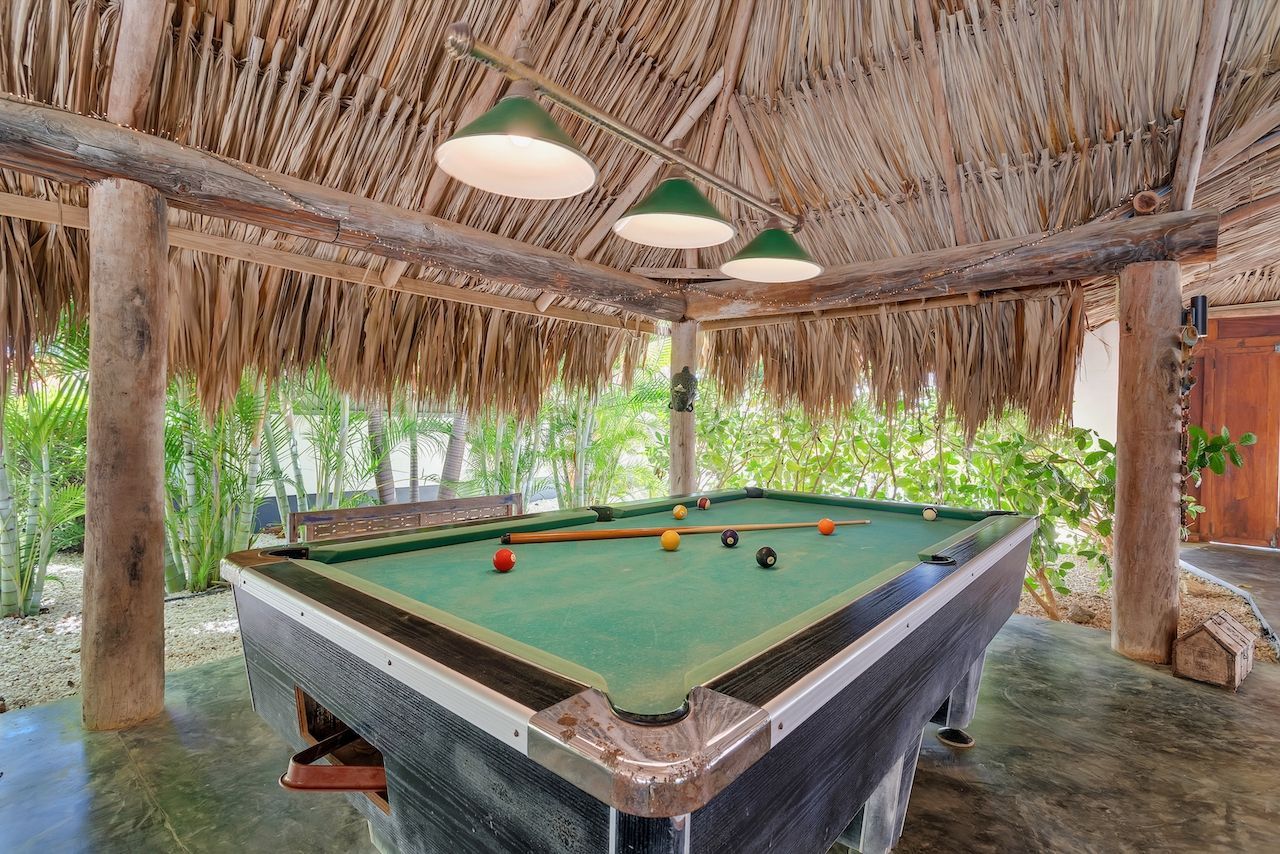 There is a pool table under a thatched roof.
