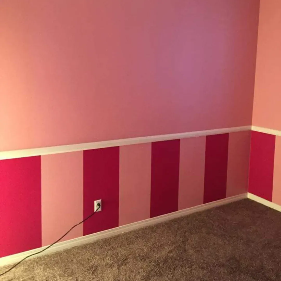 Pink bedroom corner with striped wainscoting, white trim, gray carpet, and an outlet on the wall