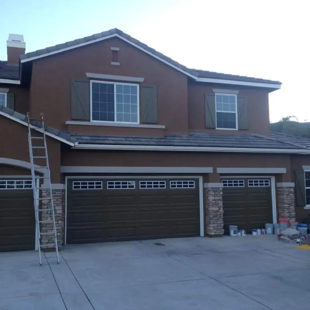 Two-story brick house with three garage doors and a ladder on the left side of the driveway