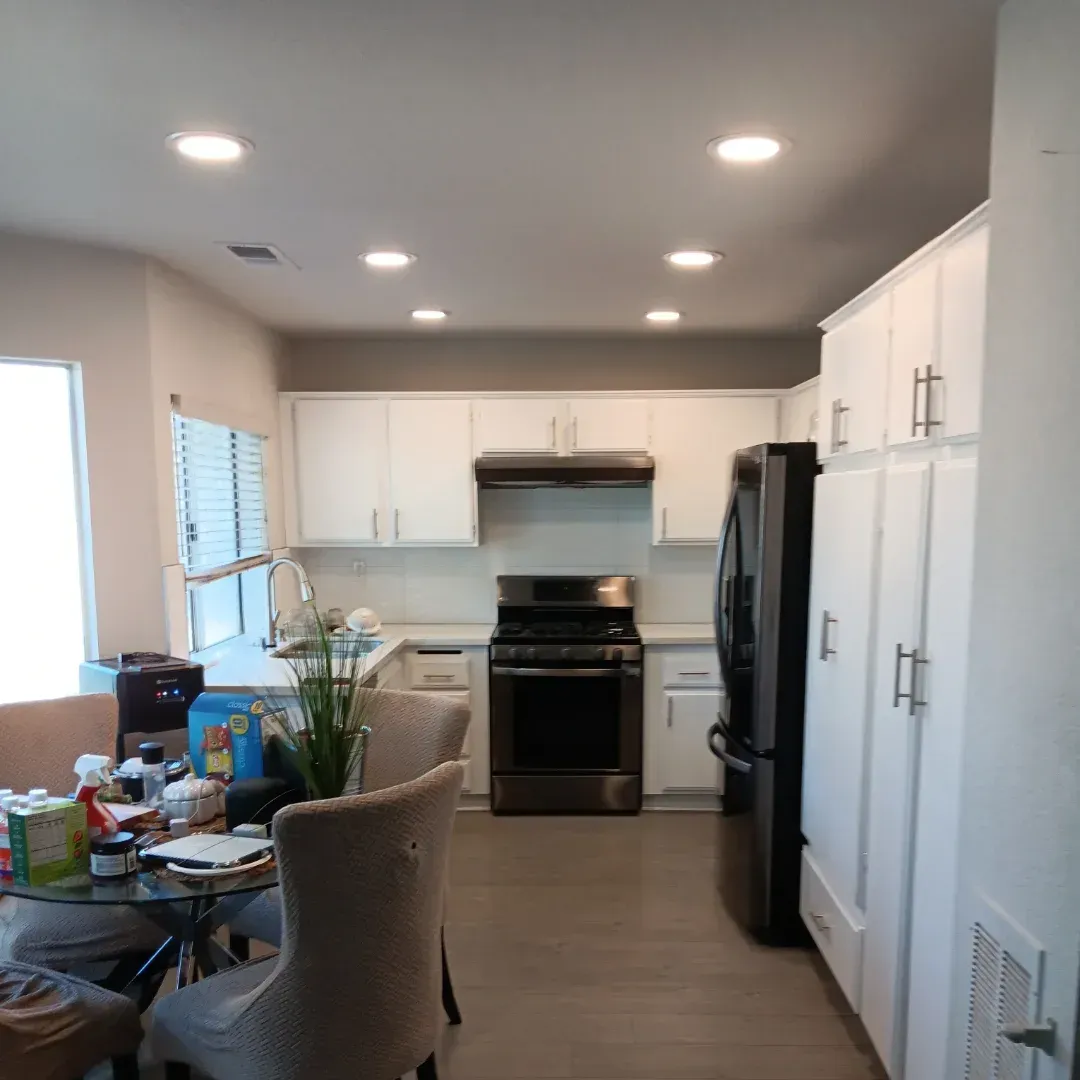Bright modern kitchen with white cabinets, black appliances, and a dining table near a window