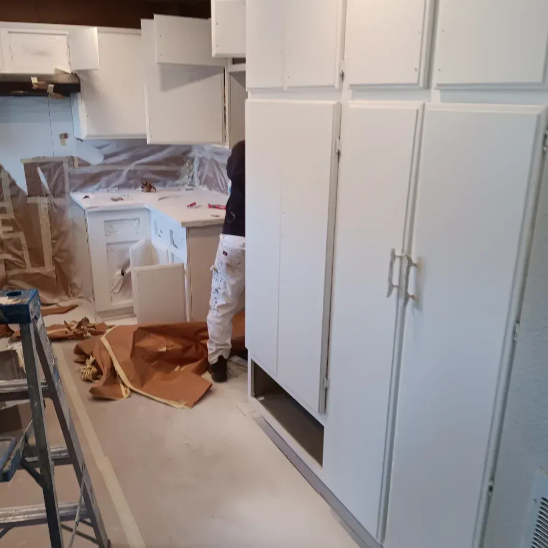 Kitchen under renovation with white cabinets, covered counters, and construction tools on the floor