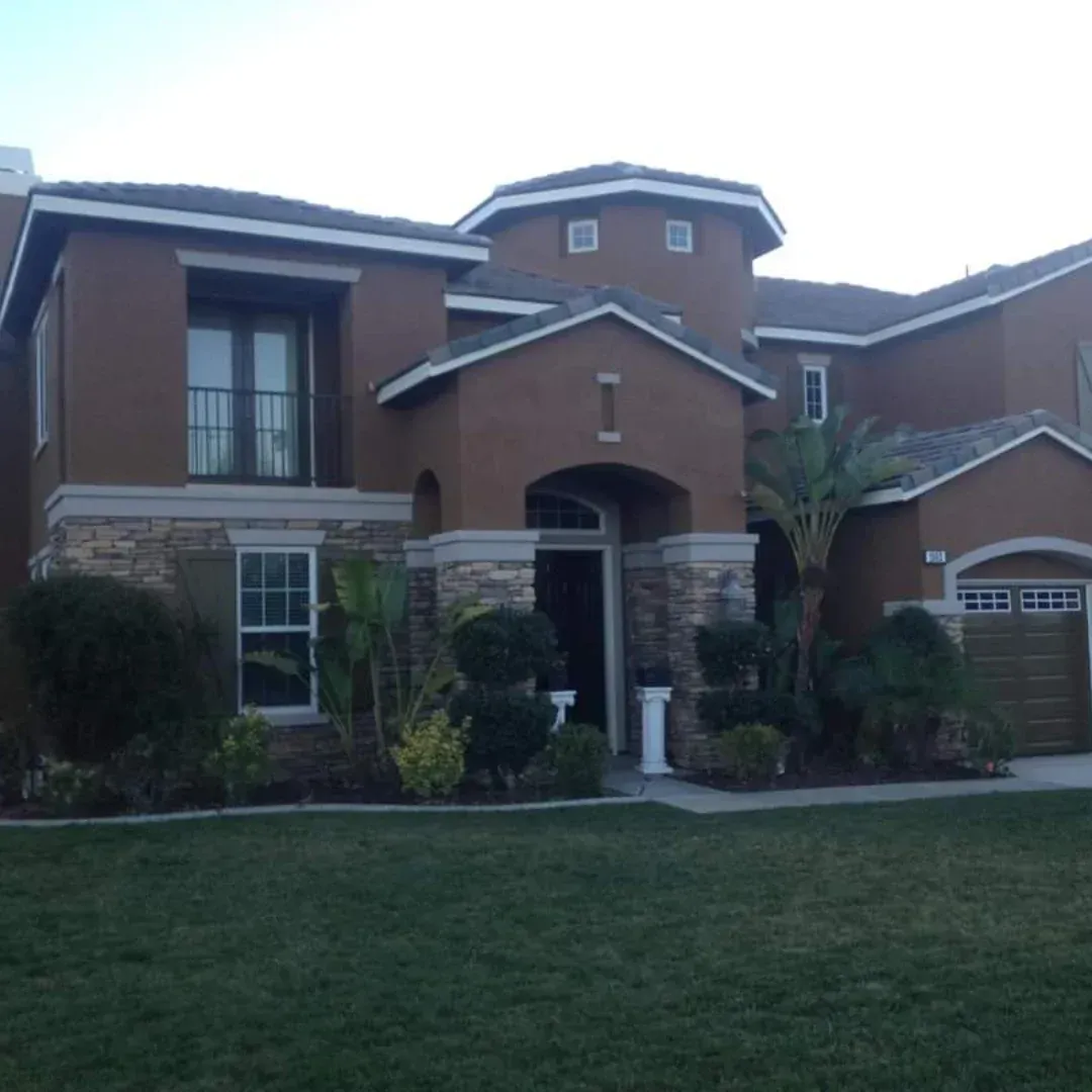 Large two-story brick house with a front lawn, arched entryway, and garage at dusk