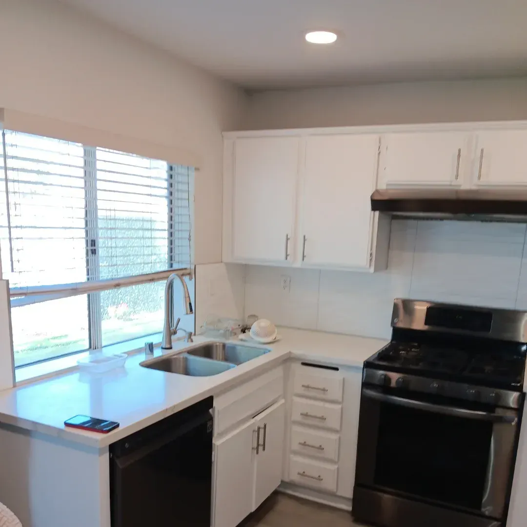 Bright white kitchen with black stove, sink by window, and white cabinets
