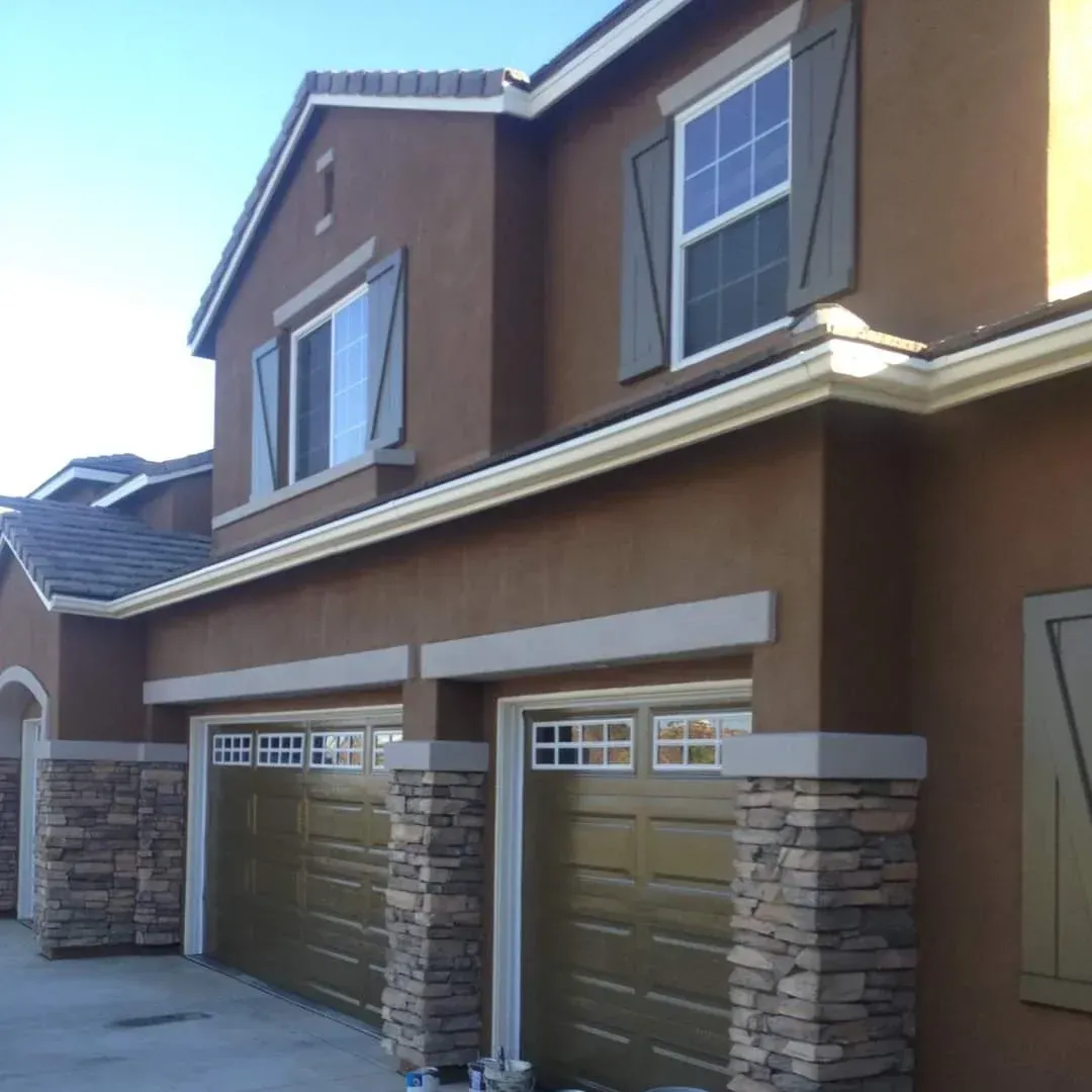 Two-story tan house with stone-accented double garage doors and white-trimmed windows