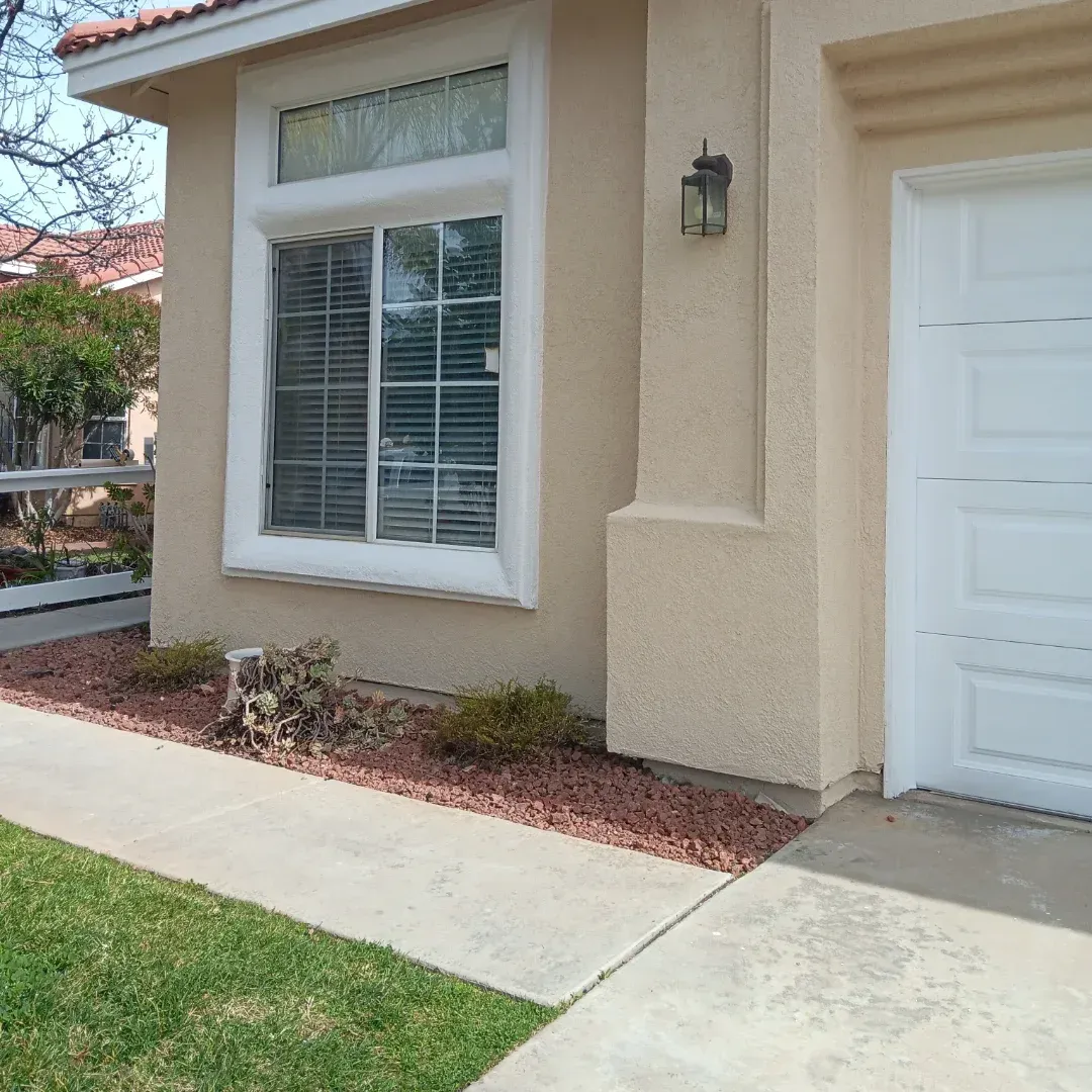 Front entrance of a beige stucco house with a white window, door, and concrete walkway