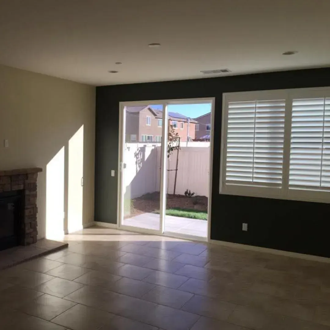 Empty living room with tile floor, sliding glass door to backyard, fireplace, and shuttered window.