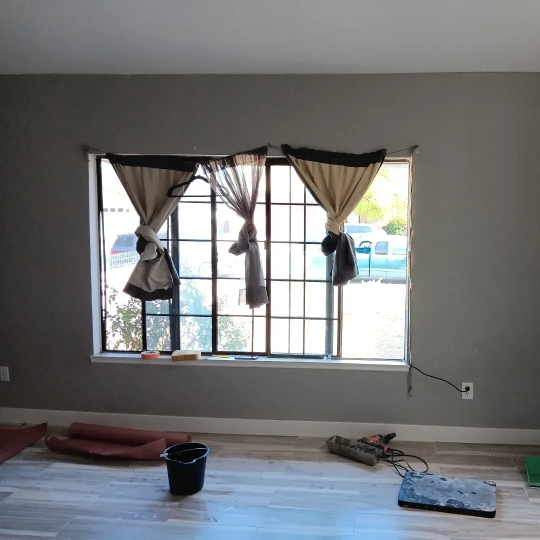 Empty room with gray walls, window curtains, and cleaning supplies on the floor.