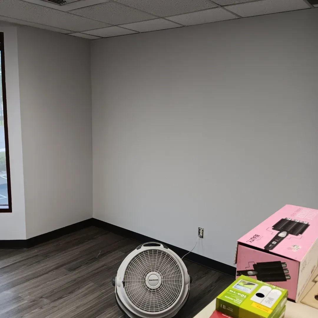 Empty office corner with a window, a floor fan, and pink and yellow boxes on the floor.