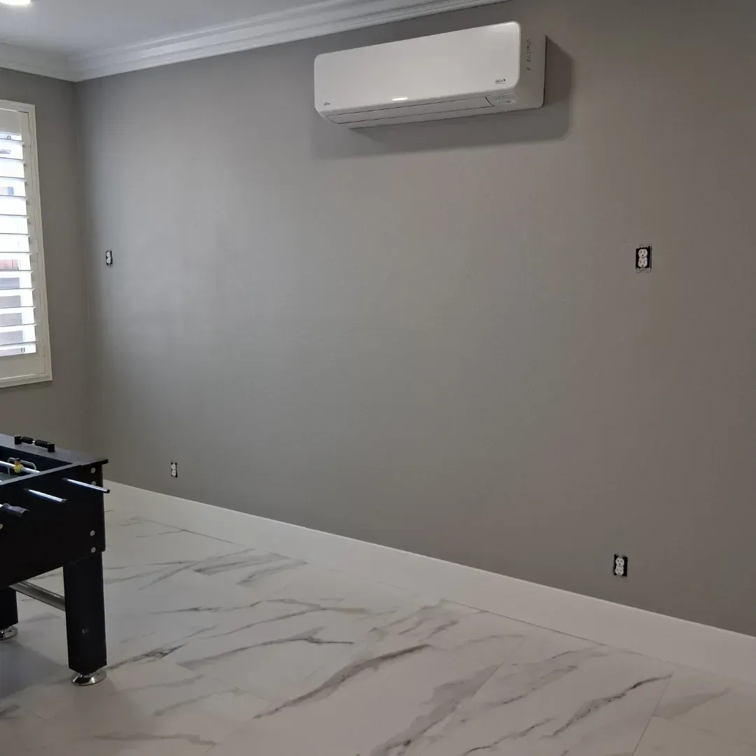 Empty room with gray walls, white marble floor, wall-mounted air conditioner, and a foosball table edge.