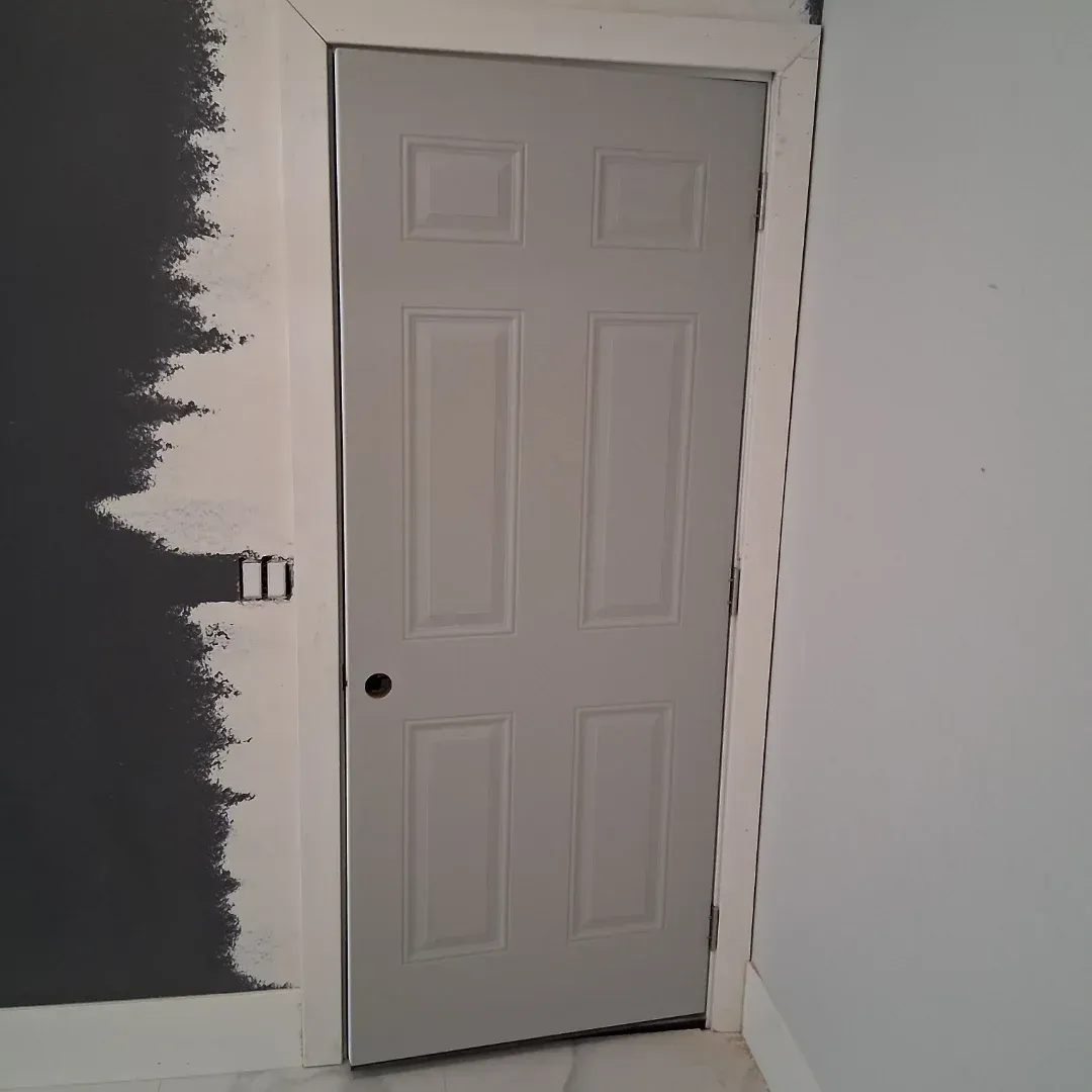 Gray interior door in an unfinished room with white walls and a black painted section on the left
