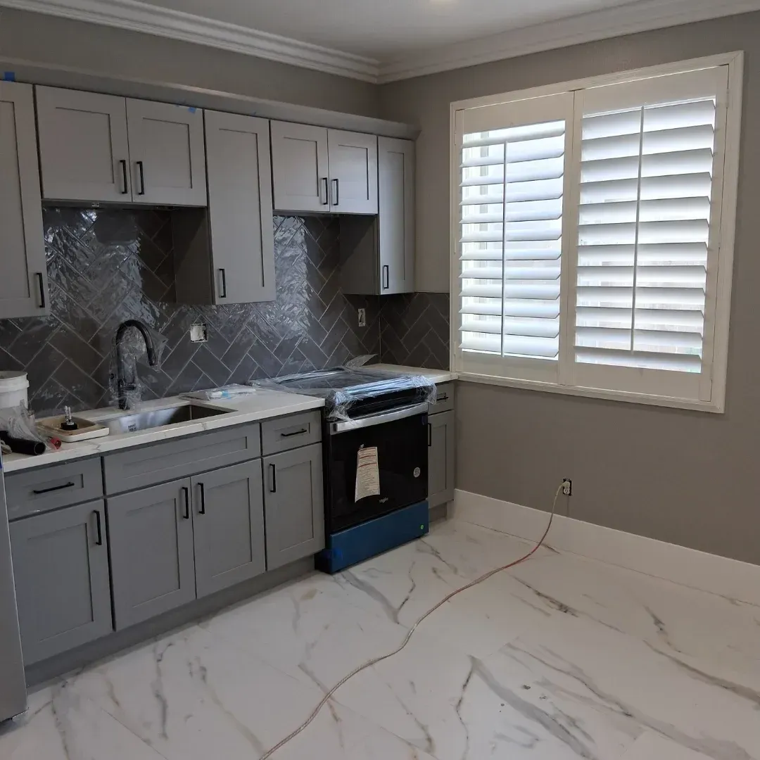 Modern kitchen with gray cabinets, marble-look floor, tile backsplash, and window shutters