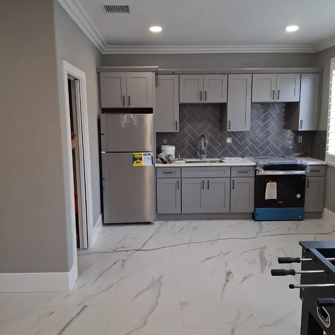 Modern kitchen with gray cabinets, stainless fridge, patterned backsplash, and white marble-look floor tiles